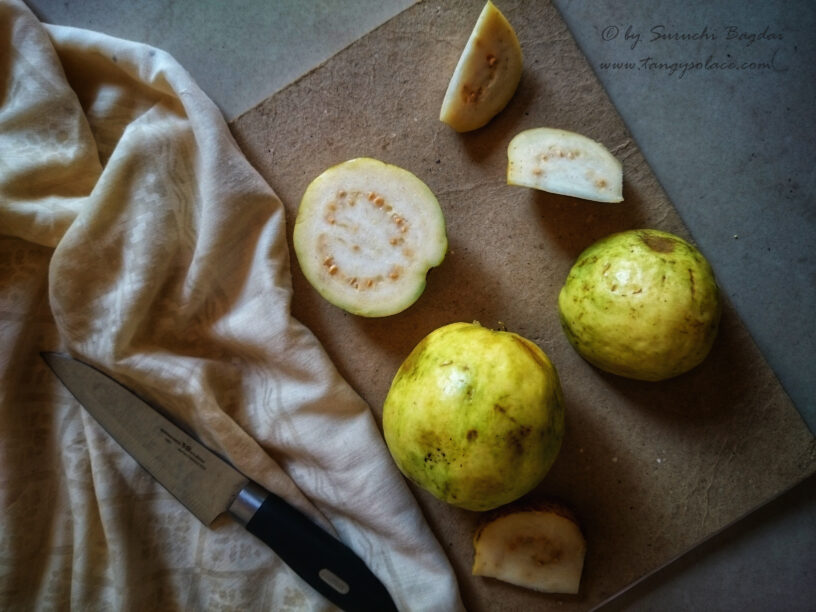 Cross sectional and whole ripe guava placed on brown and grey background with knife to the side.