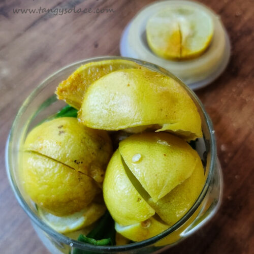 Quartered lemon and slit chillies in jar on wood background