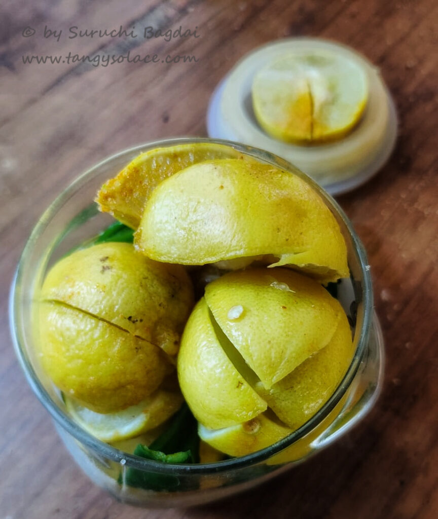 Quartered lemon and slit chillies in jar on wood background
