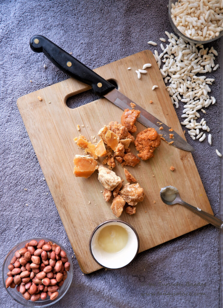 chopped jaggery on board, strewn murmura and peanut bowl on grey background