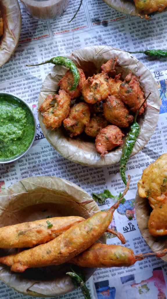 Close up photo of fried corn and mirchi bhajiyas layed out on newspaper served with green chutney 